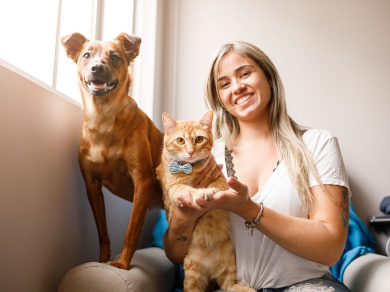 Woman smiling sitting with a dog and cat in a chair